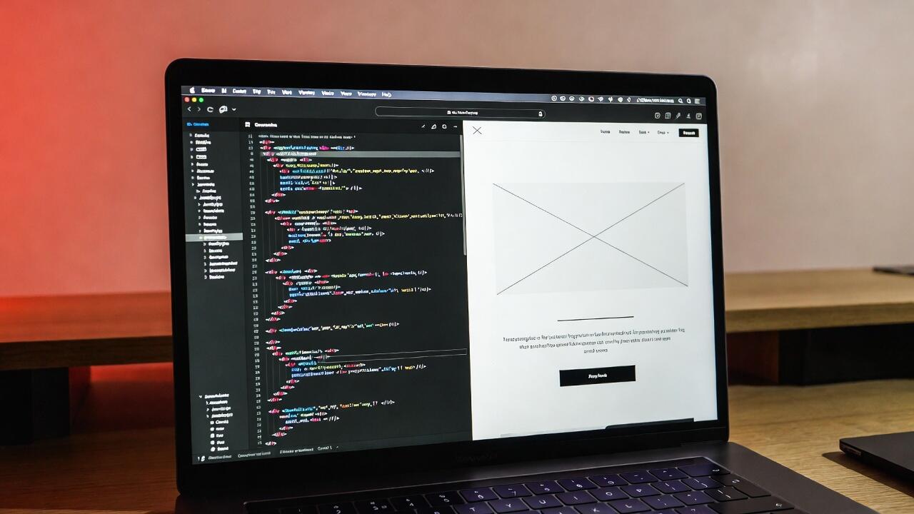 Laptop screen showing HTML code on one side and a clean website on the other